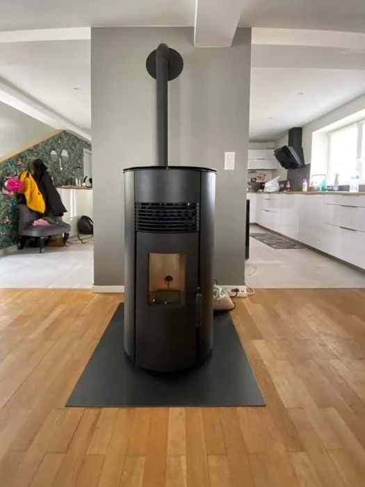 Intérieur résidentiel moderne avec poêle à bois cylindrique noir installé au centre d'un espace ouvert reliant salon et cuisine