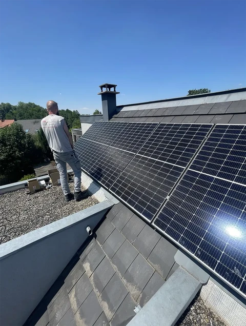 Ouvrier en tenue blanche installant des panneaux solaires photovoltaïques sur toiture résidentielle par temps ensoleillé
