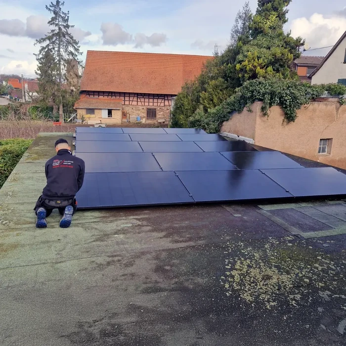Ouvrier installant des panneaux photovoltaïques sur toiture plate, environnement résidentiel européen avec maisons traditionnelles