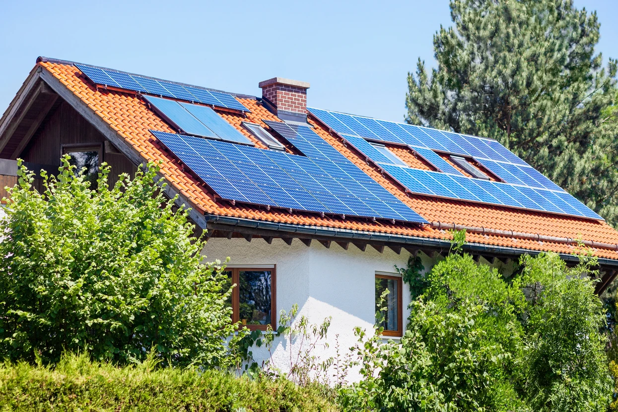 Vieille maison avec panneaux solaires sur toit en tuiles avec jardin vert en côté Country