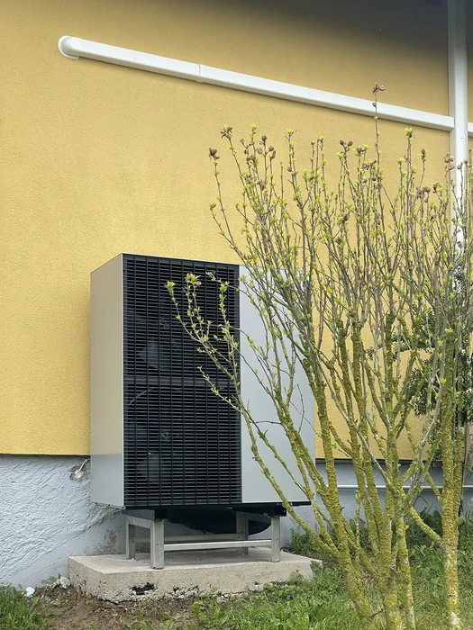 Extérieur résidentiel avec unité de pompe à chaleur air-eau installée sur dalle béton contre mur jaune