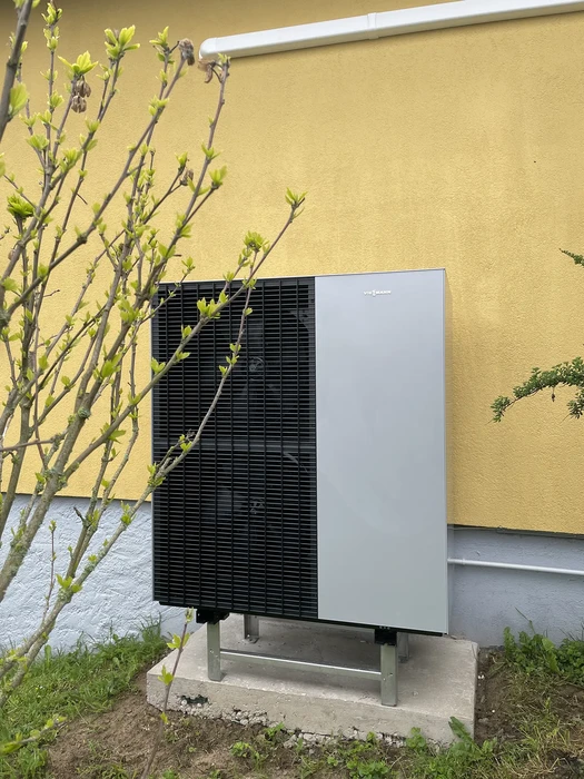 Extérieur résidentiel avec pompe à chaleur air-eau installée sur dalle béton contre mur jaune
