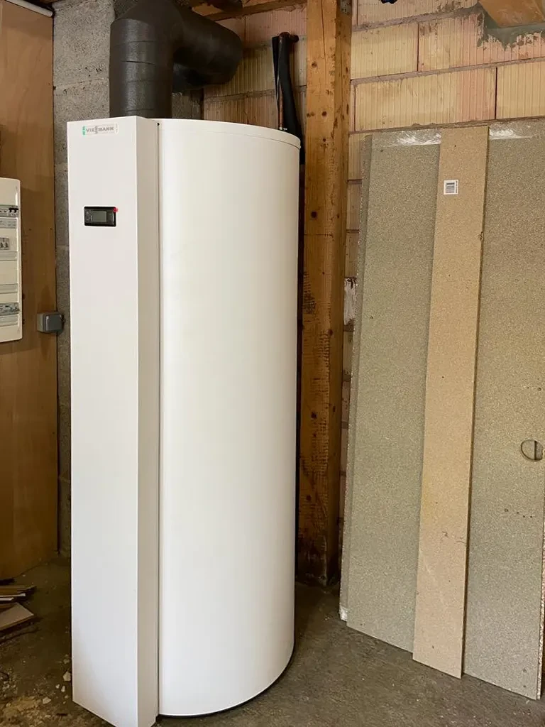 Cave ou sous-sol avec chauffe-eau électrique cylindrique blanc installé contre mur en blocs de béton