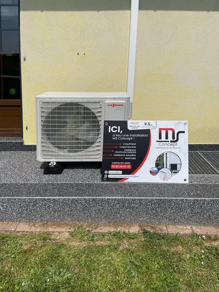 Extérieur d'un bâtiment résidentiel avec unité extérieure de climatisation installée au sol contre un mur bicolore jaune et beige